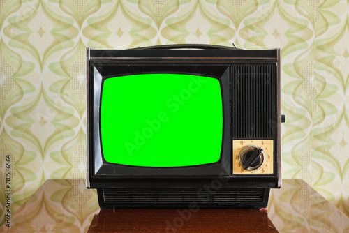 An old TV with a green screen on the nightstand against the background of wallpaper.