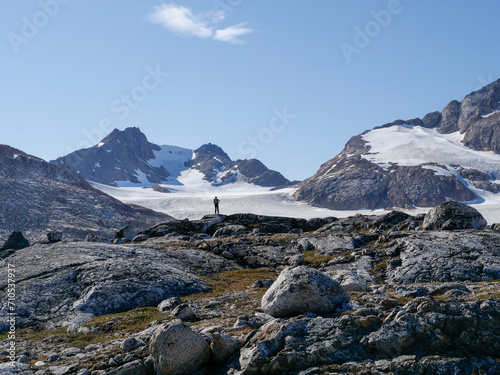 A mountaineer stands in a Greenlandic rocky landscape and looks out over a glacier.