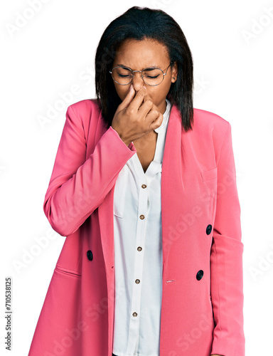 Beautiful hispanic woman wearing business jacket smelling something stinky and disgusting, intolerable smell, holding breath with fingers on nose. bad smell