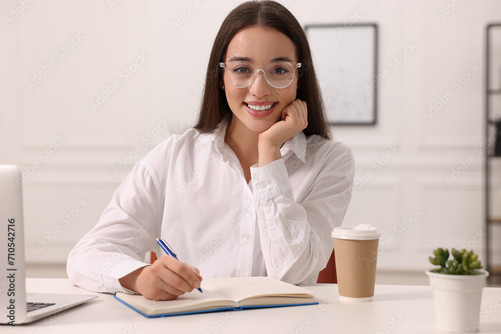 Young woman writing in notebook at white table indoors Young woman writing in notebook at white table indoors