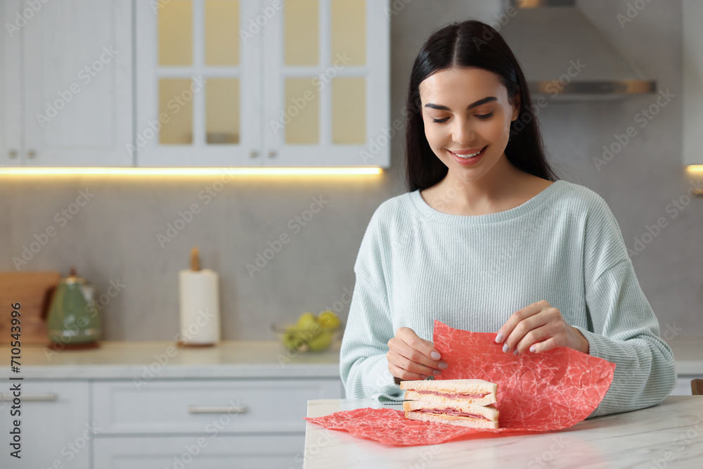 Happy woman packing sandwich into beeswax food wrap at table in kitchen Happy woman packing sandwich into beeswax food wrap at table in kitchen