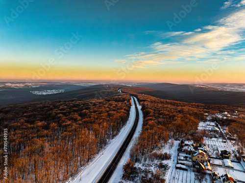 aerial view of the treetops of the forest and a road illuminated by the setting sun during winter in moldova