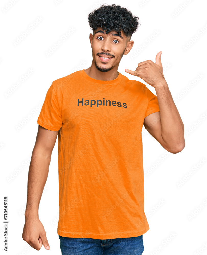 Young arab man wearing tshirt with happiness word message smiling doing phone gesture with hand and fingers like talking on the telephone. communicating concepts. Young arab man wearing tshirt with happiness word message smiling doing phone gesture with hand and fingers like talking on the telephone. communicating concepts.