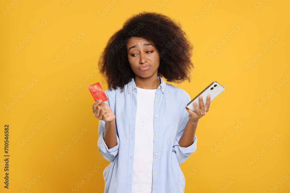 Confused woman with credit card and smartphone on orange background. Debt problem - obrazy, fototapety, plakaty 