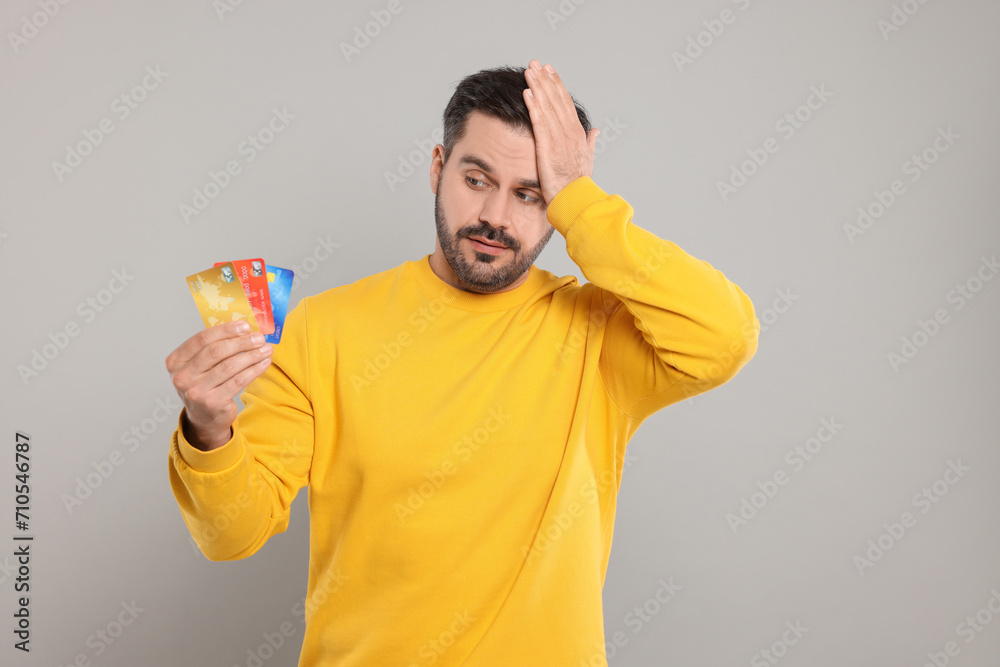 Confused man with credit cards on grey background. Debt problem Confused man with credit cards on grey background. Debt problem