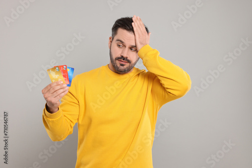 Confused man with credit cards on grey background. Debt problem