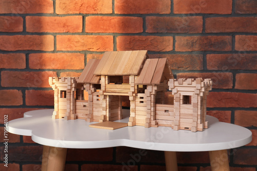 Wooden gate on white table near brick wall. Children s toy