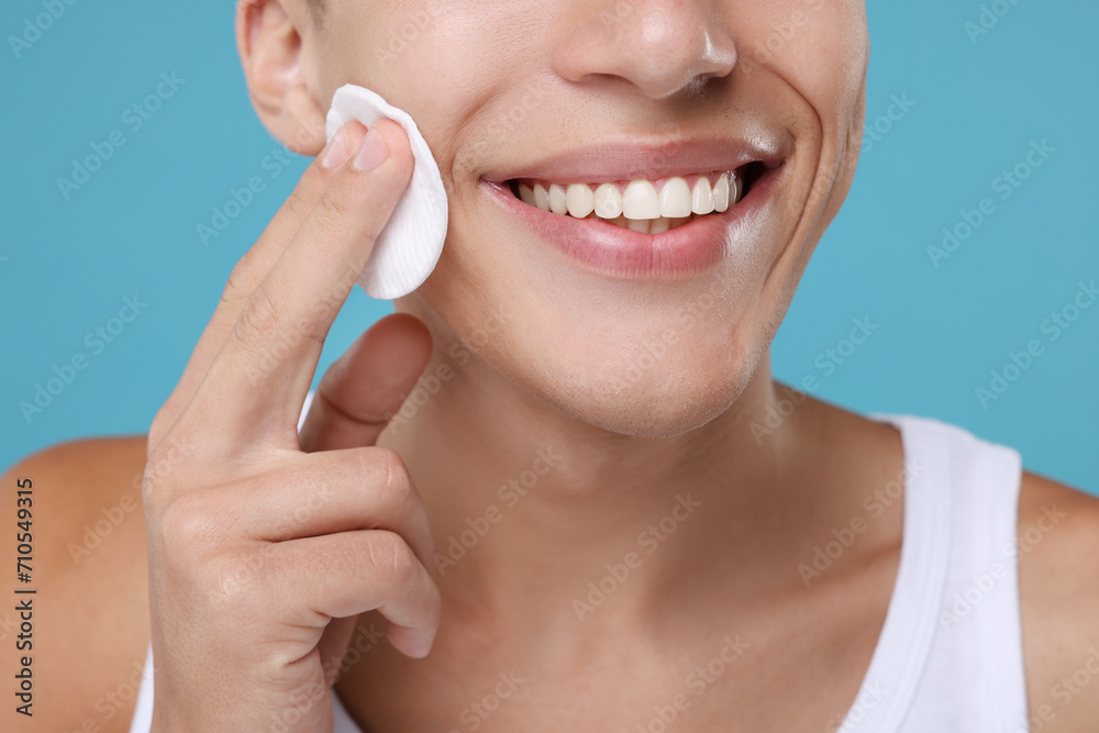 Man cleaning face with cotton pad on light blue background, closeup Man cleaning face with cotton pad on light blue background, closeup