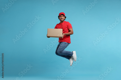 Happy young courier with parcel jumping on light blue background