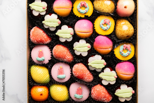 Box of rainbow marzipan sweets in form of different fruits and cakes photo