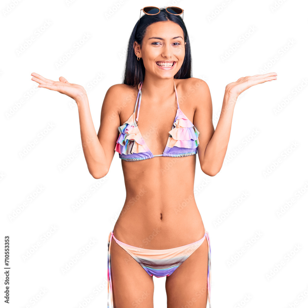 Fototapeta premium Young beautiful latin girl wearing bikini and sunglasses celebrating crazy and amazed for success with arms raised and open eyes screaming excited. winner concept