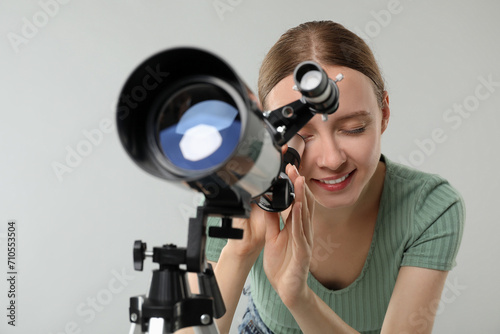 Young astronomer looking at stars through telescope on grey background