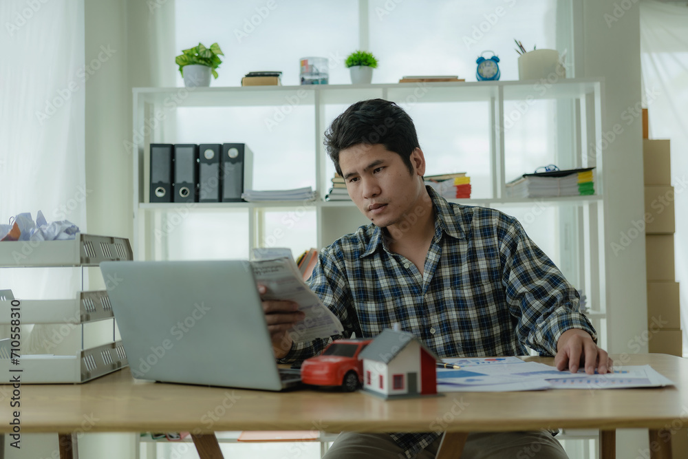 Young Asian man calculates car payments Home installments in financial planning and income Asset approval concepts, buying cars and houses, checklist, home loans, home taxes Young Asian man calculates car payments Home installments in financial planning and income Asset approval concepts, buying cars and houses, checklist, home loans, home taxes