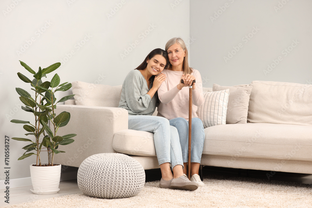 Mature lady with walking cane and young woman on sofa at home Mature lady with walking cane and young woman on sofa at home