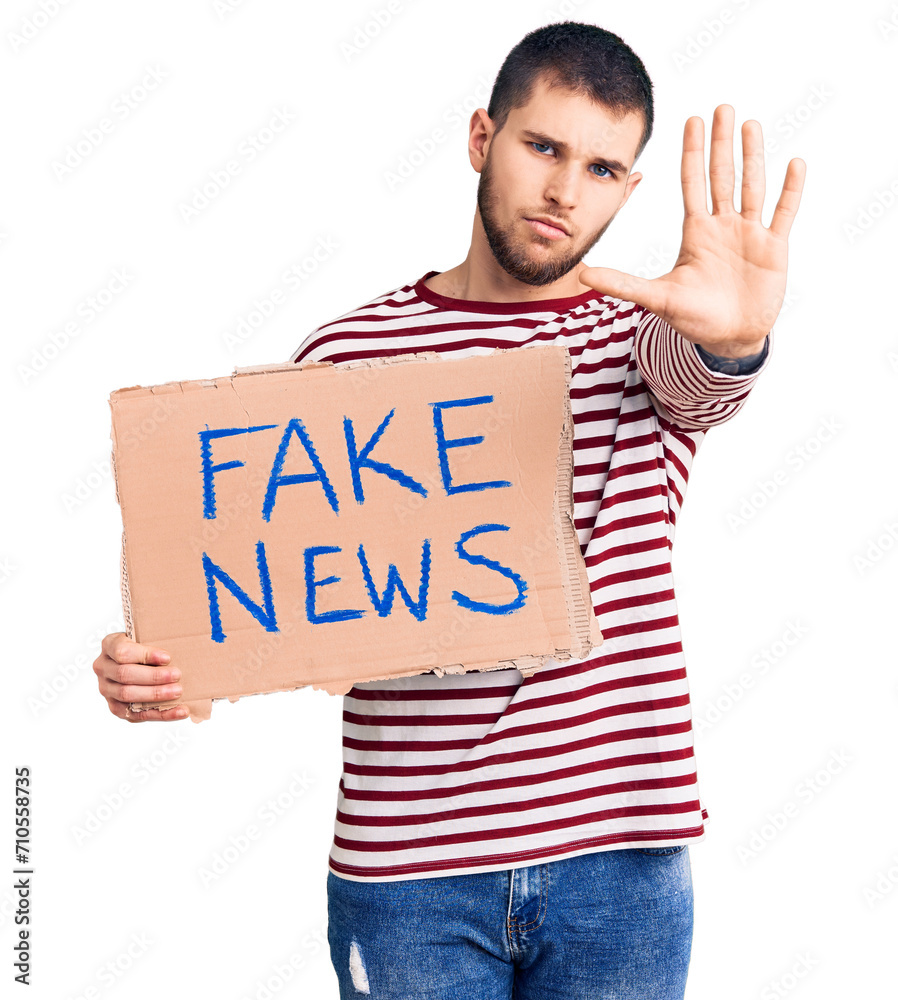 Young handsome man holding fake news message banner with open hand doing stop sign with serious and confident expression, defense gesture Young handsome man holding fake news message banner with open hand doing stop sign with serious and confident expression, defense gesture