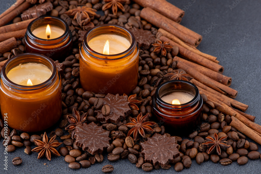 Soy scented candle in a jar. Coffee beans, anise, cinnamon spices. The candles are burning. Dark background Soy scented candle in a jar. Coffee beans, anise, cinnamon spices. The candles are burning. Dark background
