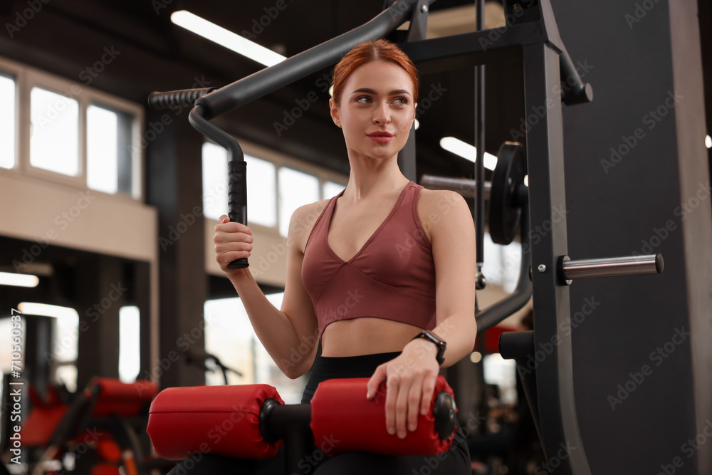 Fototapeta premium Athletic young woman training with lat pulldown machine in gym