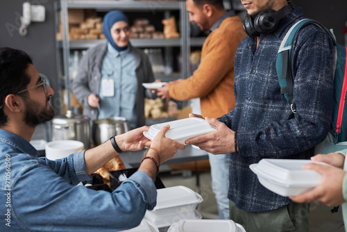 Side view closeup of volunteer giving free food to Middle Eastern refugees standing in line at soup kitchen