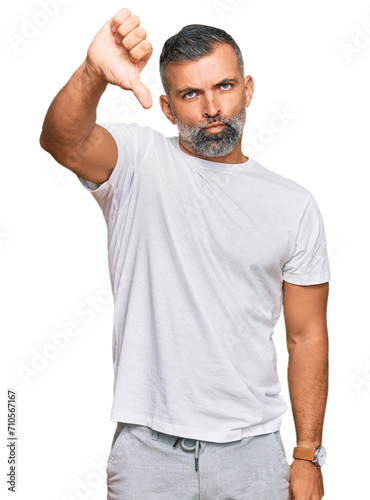 Middle age handsome man wearing casual white tshirt looking unhappy and angry showing rejection and negative with thumbs down gesture. bad expression.