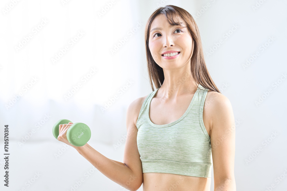 Naklejka premium 自宅でダンベルトレーニングをするアジア人女性