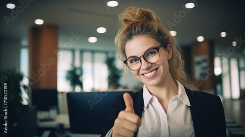 Young woman at the office doing happy thumbs up gesture with hand. approving expression looking at the camera showing success.