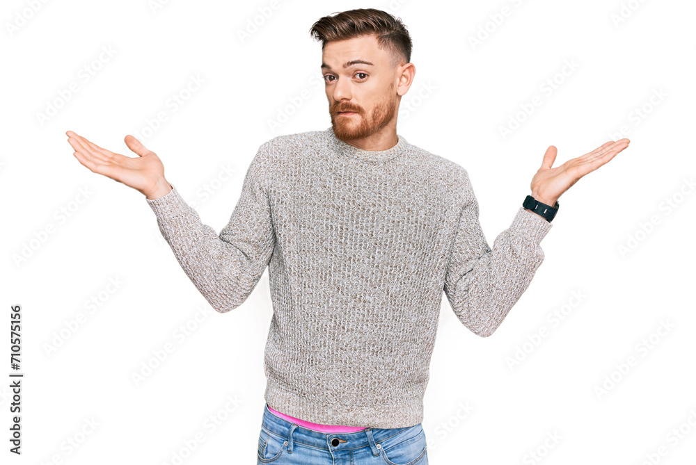 Young redhead man wearing casual winter sweater clueless and confused expression with arms and hands raised. doubt concept. Young redhead man wearing casual winter sweater clueless and confused expression with arms and hands raised. doubt concept.