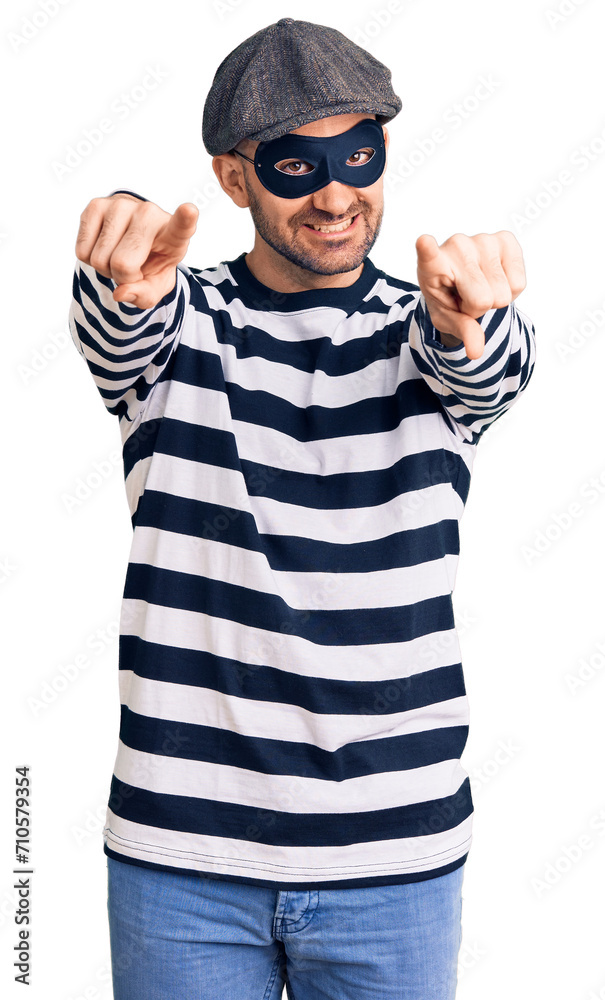 Young handsome man wearing burglar mask pointing to you and the camera with fingers, smiling positive and cheerful Young handsome man wearing burglar mask pointing to you and the camera with fingers, smiling positive and cheerful