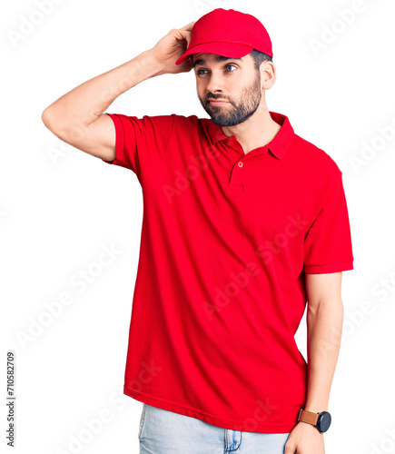 Young handsome man with beard wearing delivery uniform confuse and wondering about question. uncertain with doubt, thinking with hand on head. pensive concept.
