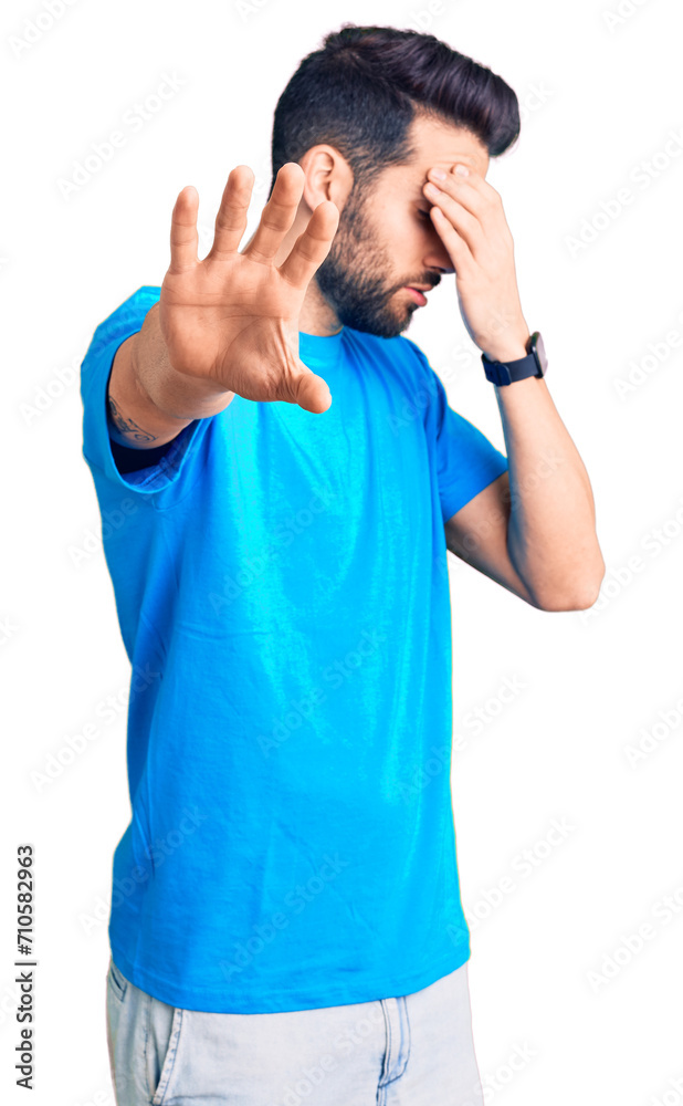 Young handsome man with beard wearing casual t-shirt covering eyes with hands and doing stop gesture with sad and fear expression. embarrassed and negative concept.