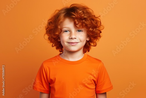 Cute handsome little boy with curly red hair and freckles wearing an orange T-shirt on an orange background. Place for text. Studio portrait of happy red-haired child