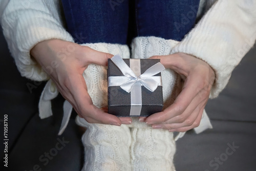 A gray gift box with a wyite bow that a girl holds in her palms.
