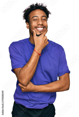 Young african american man with beard wearing casual purple t shirt looking confident at the camera smiling with crossed arms and hand raised on chin. thinking positive.