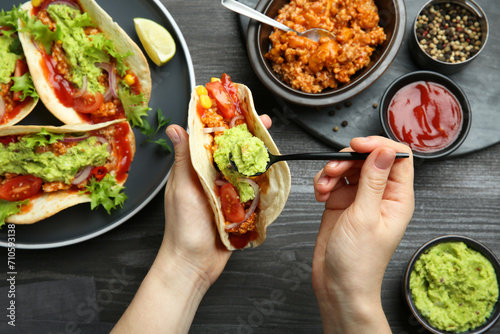 Woman adding guacamole to delicious taco at wooden table, top view photo