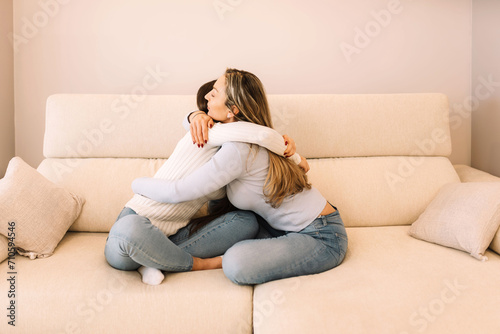 mother and teenage daughter sitting together on couch in embrace. Trusted relationships between mom and teen girl