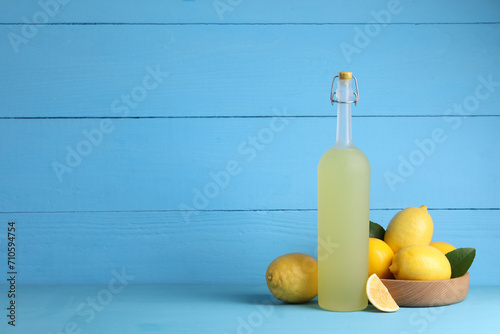 Fotografi Bottle of tasty limoncello liqueur, lemons and green leaves on light blue table,