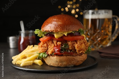 Delicious burger with crispy chicken patty and french fries on black table