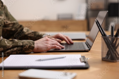 Military service. Soldier working with laptop at wooden table indoors, closeup photo