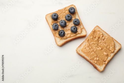 Delicious toasts with peanut butter and blueberries on white marble table, flat lay. Space for text