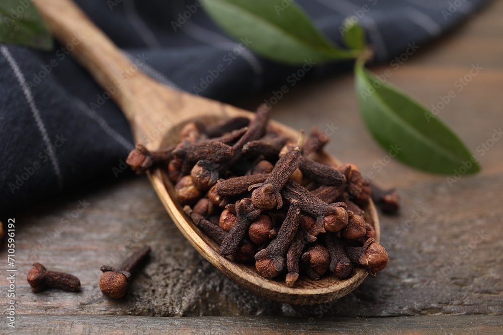 Fototapeta premium Spoon with aromatic cloves on wooden table, closeup