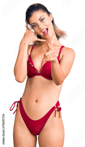 Young beautiful woman wearing bikini smiling doing talking on the telephone gesture and pointing to you. call me. © Krakenimages.com
