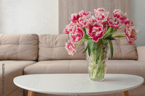 Vase of pink tulips on coffee table with blurred background of beige modern cozy light living room. Copy space