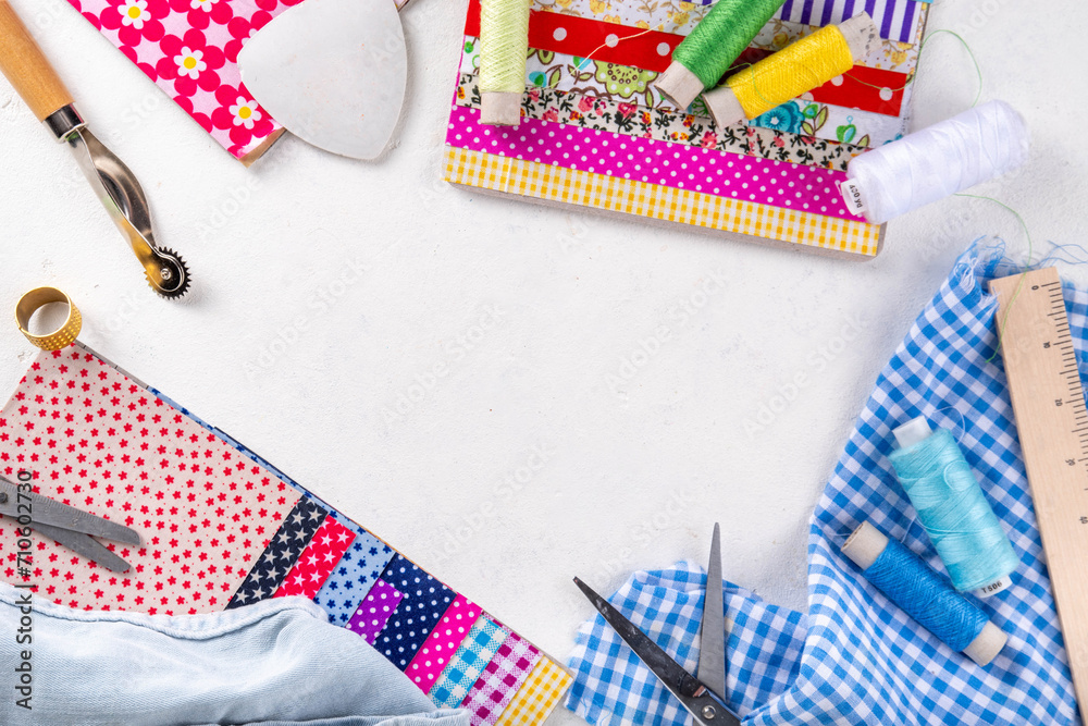 Fototapeta premium Sewing, needlework and clothing repair, background, scrapbooking, quilting. Colorful pieces of fabric, scissors, ruler, sewing tools, needles, threads on a white table background top view copy space