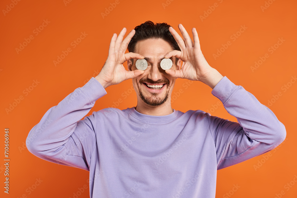 happy man holding bitcoins over his eyes and smiling at camera on orange background, cryptocurrency happy man holding bitcoins over his eyes and smiling at camera on orange background, cryptocurrency