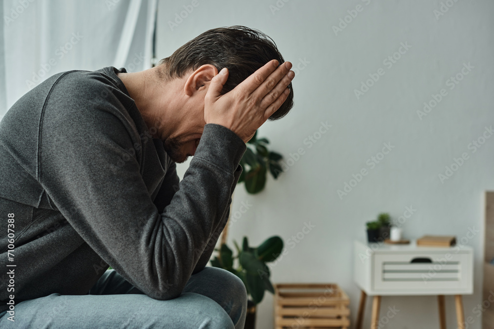 Obraz premium upset bearded man in casual home wear sitting on bedroom bench and covering face with hands