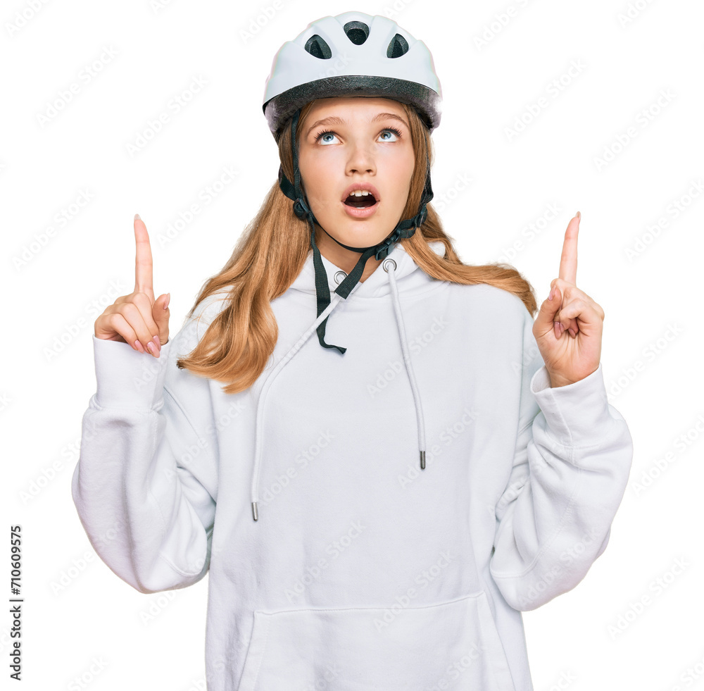 Beautiful young caucasian girl wearing bike helmet amazed and surprised looking up and pointing with fingers and raised arms. Beautiful young caucasian girl wearing bike helmet amazed and surprised looking up and pointing with fingers and raised arms.