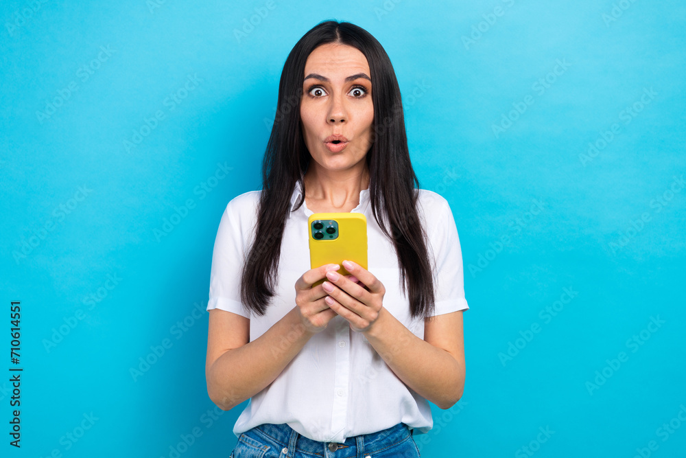 Photo of sweet impressed girl dressed white shirt smiling reading news modern device isolated blue color background Photo of sweet impressed girl dressed white shirt smiling reading news modern device isolated blue color background