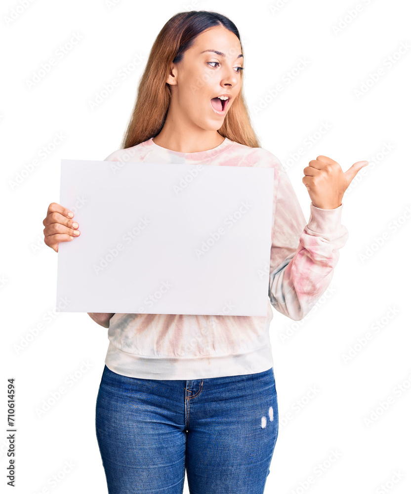 Beautiful young woman holding blank empty banner pointing thumb up to the side smiling happy with open mouth Beautiful young woman holding blank empty banner pointing thumb up to the side smiling happy with open mouth