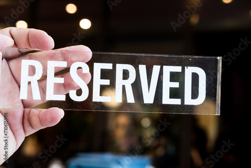 Reserved sign transparent glass tag on hand for booking seats. Arranged restaurant seats concept