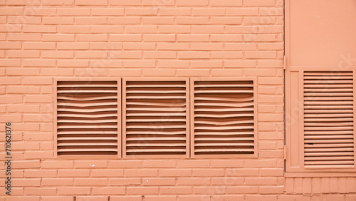 Rejilla de ventilación y ventanas en pared rosa de callejón urbano