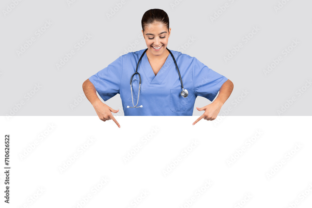 Happy lady nurse in blue uniform pointing downwards to an empty white space, ideal for advertising Happy lady nurse in blue uniform pointing downwards to an empty white space, ideal for advertising